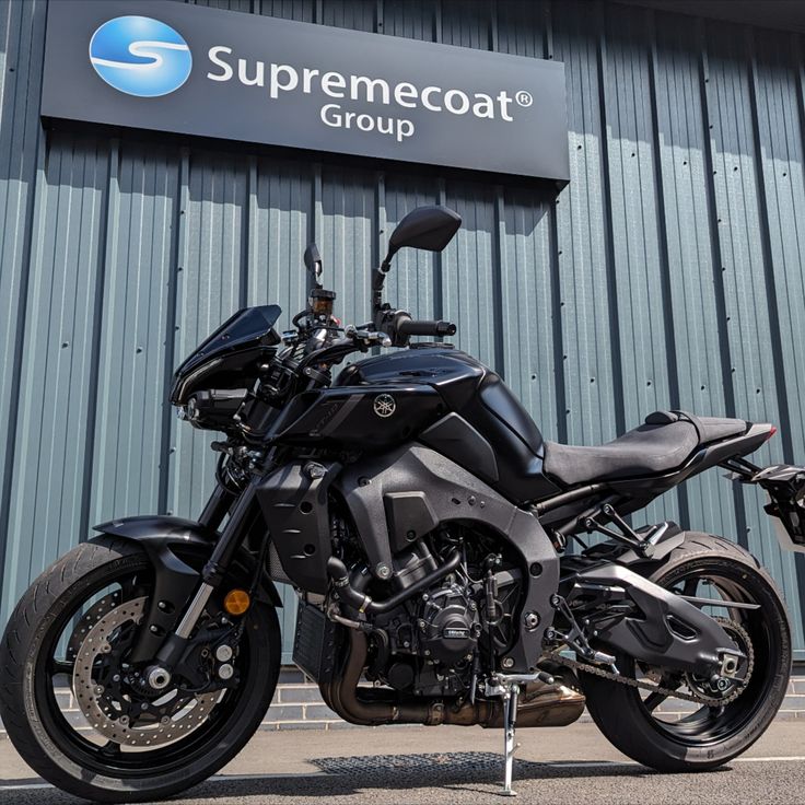 a black motorcycle parked in front of a metal building with a sign that says supremecoat group