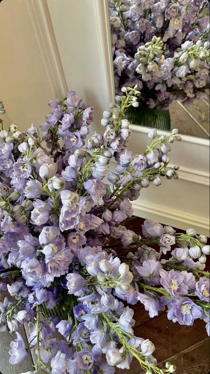 a bunch of purple flowers sitting on top of a wooden table next to a mirror