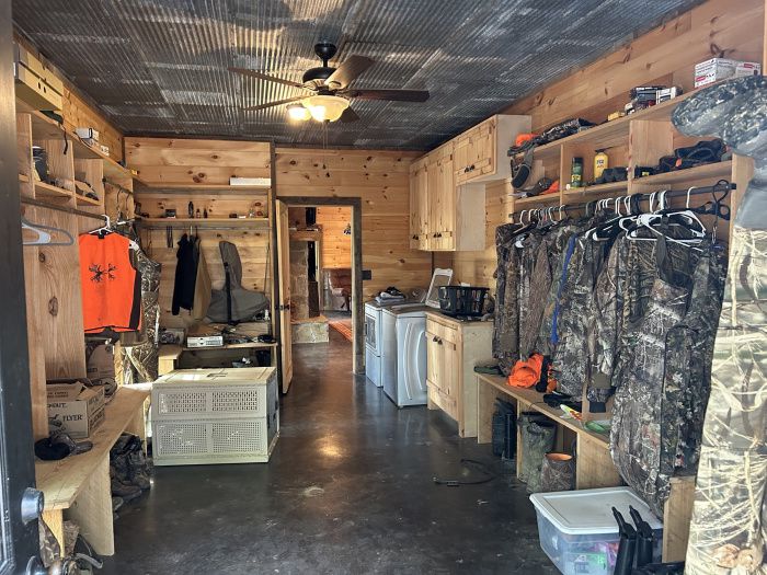 the inside of a hunting lodge with lots of items on shelves and clothes hanging up