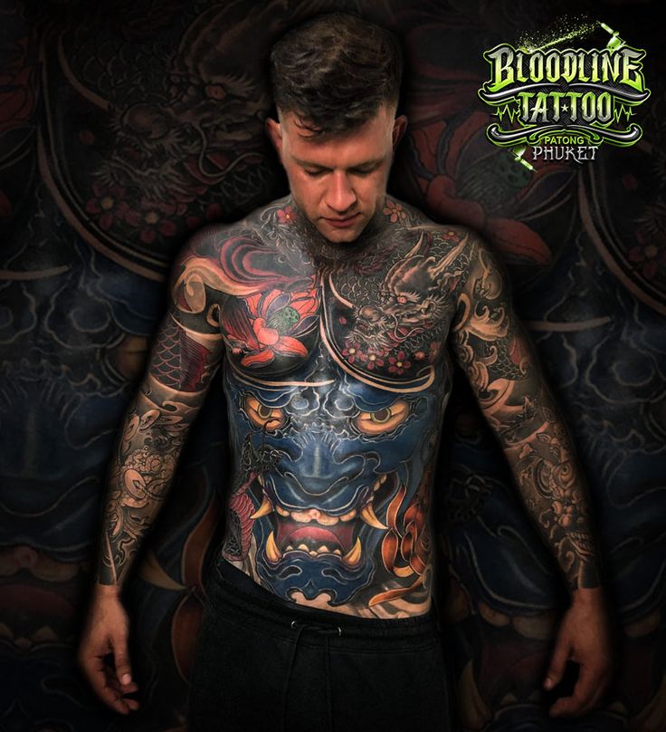 a man with tattoos standing in front of a dark background and looking at the camera