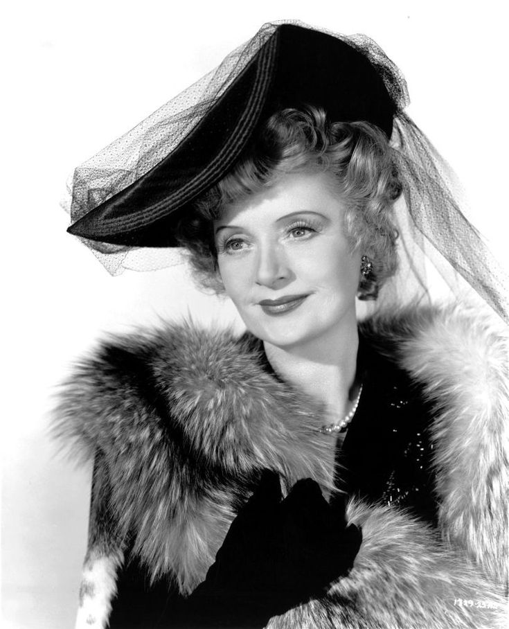 a black and white photo of a woman in a fur coat with a veil on her head