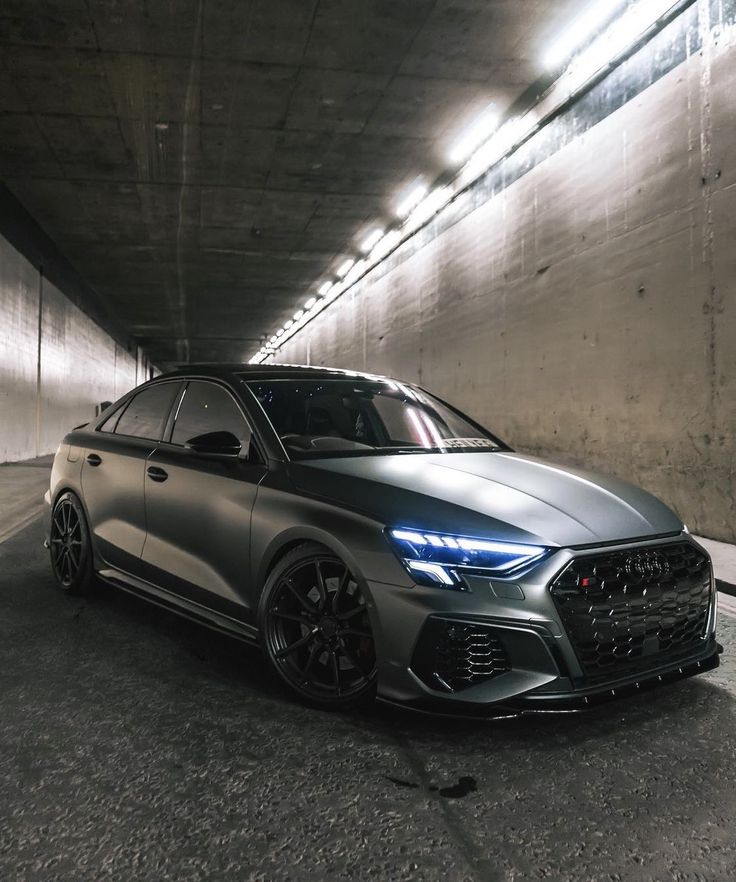 a grey car is parked in an underground parking garage with its lights on and it's hood up