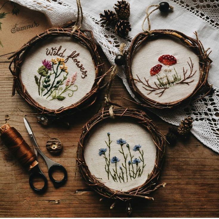 three cross stitch hoops with flowers and words on them, sitting next to a pair of scissors