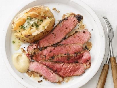 a white plate topped with meat and potatoes next to a fork, knife and spoon