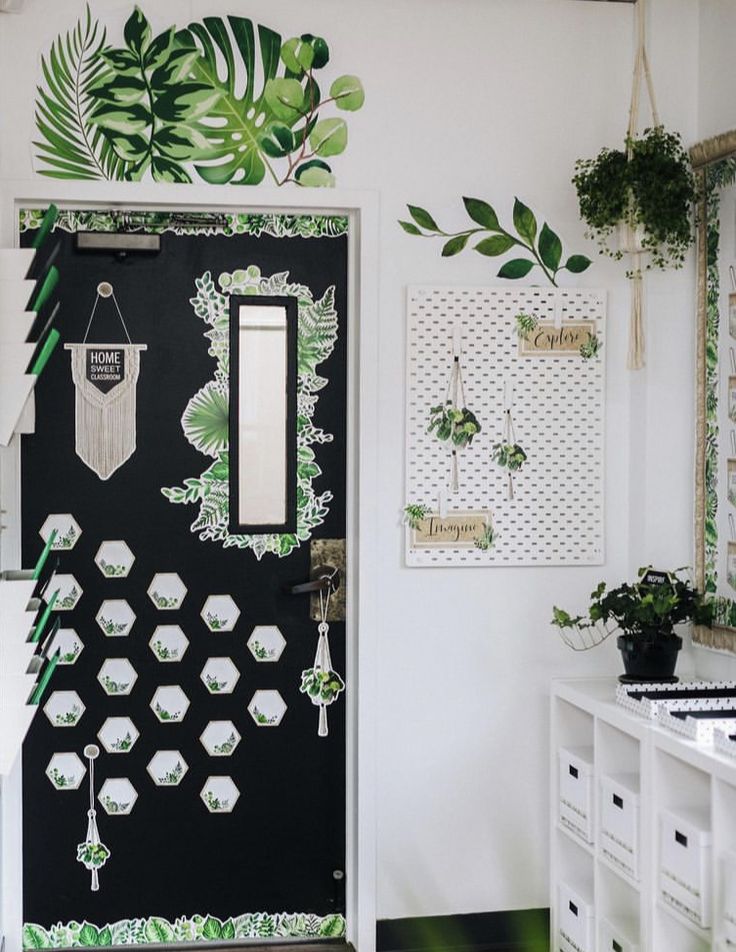 a black door decorated with green leaves and hanging plants on the wall next to it