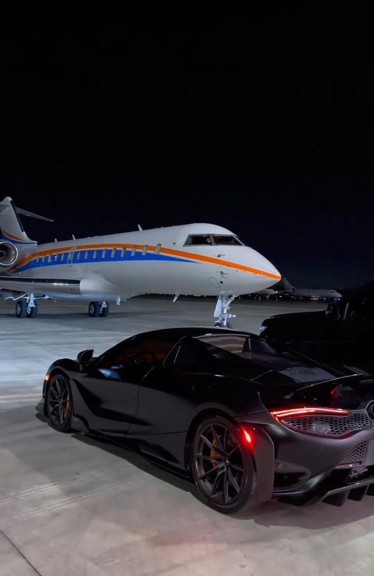 a black sports car is parked in front of an airplane at night with the jet behind it