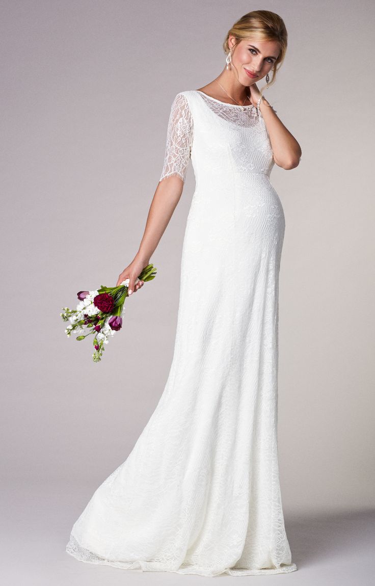 a woman in a long white dress holding a flower bouquet and posing for the camera