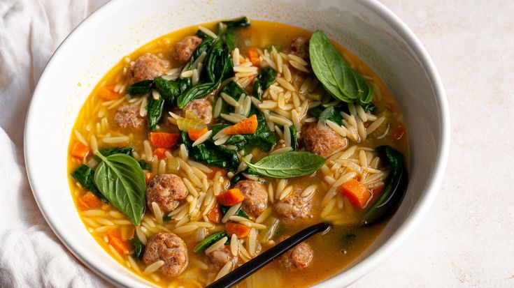 a bowl of pasta soup with meatballs and spinach leaves on the side, ready to be eaten