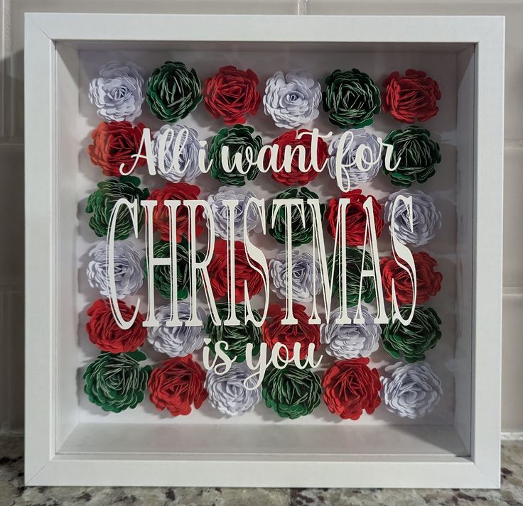 a white frame with red, green and white paper flowers in the center that says all i want for christmas is you