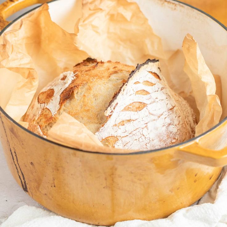 a loaf of bread sitting inside of a yellow pot on top of a white towel