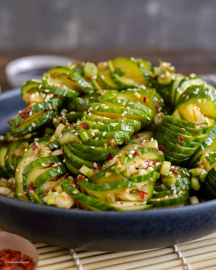 a blue bowl filled with green vegetables on top of a bamboo mat