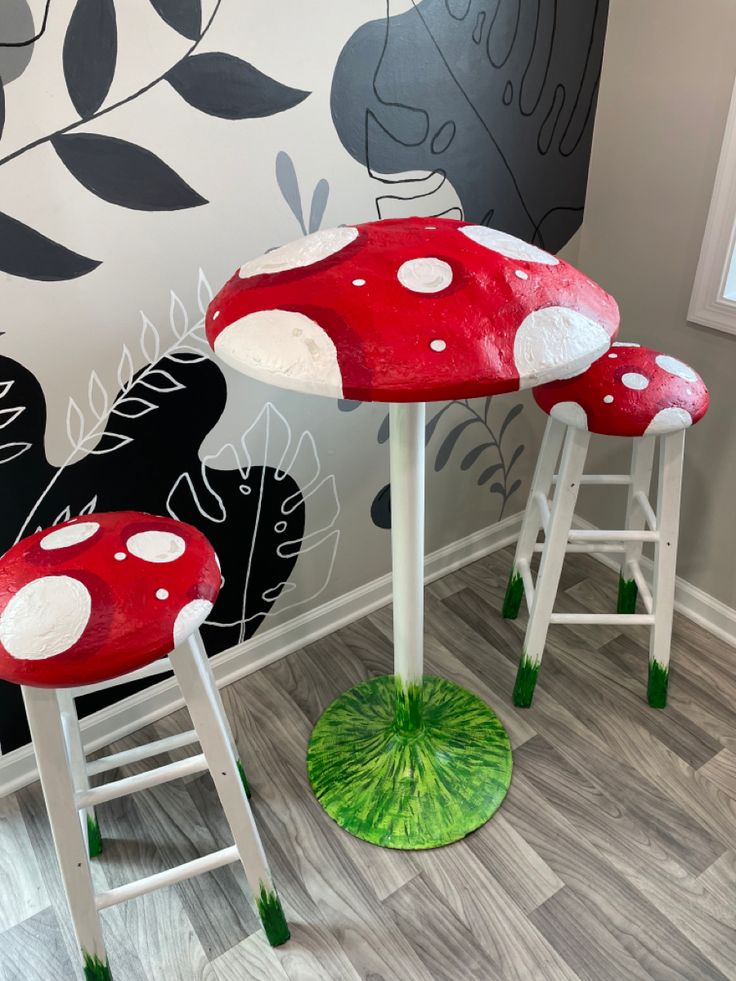 two stools with red mushrooms on them in front of a wall painted with black and white designs