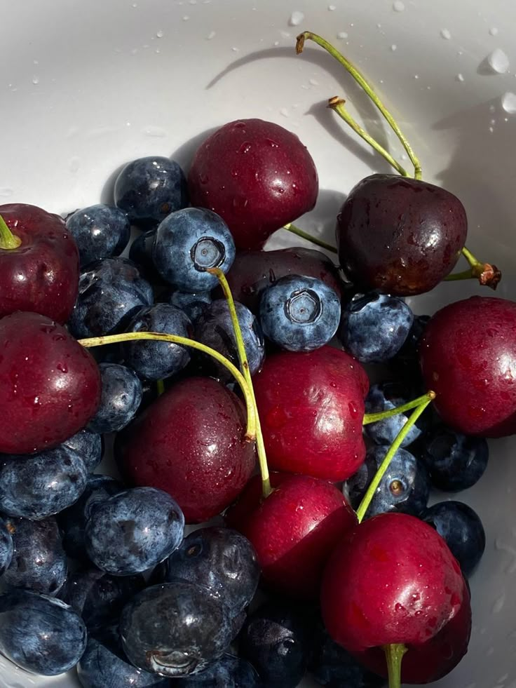 blueberries and cherries in a white bowl with water droplets