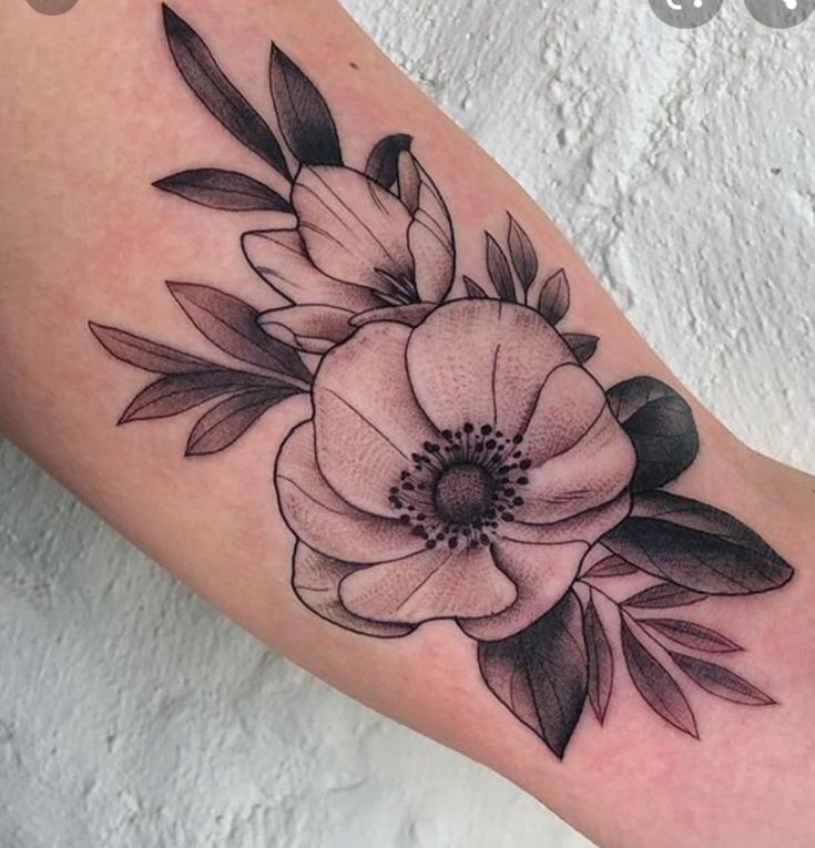 a black and white flower tattoo on the right arm, with leaves around it's center