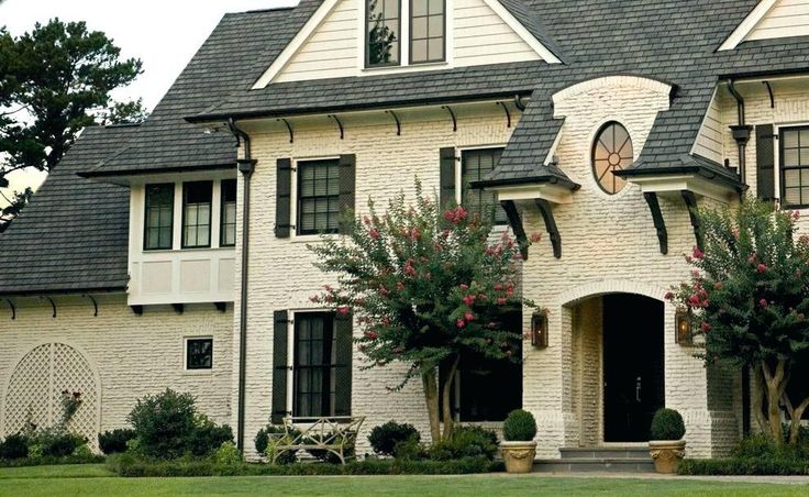 a large white brick house with black shutters and two story windows on the front