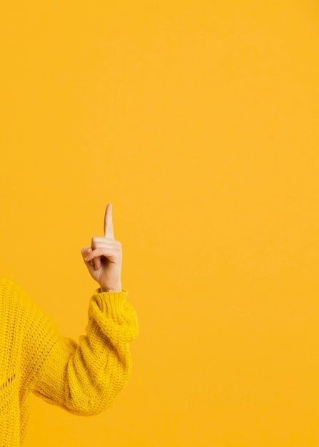 a woman in a yellow sweater is holding her hand up to the side and pointing at something