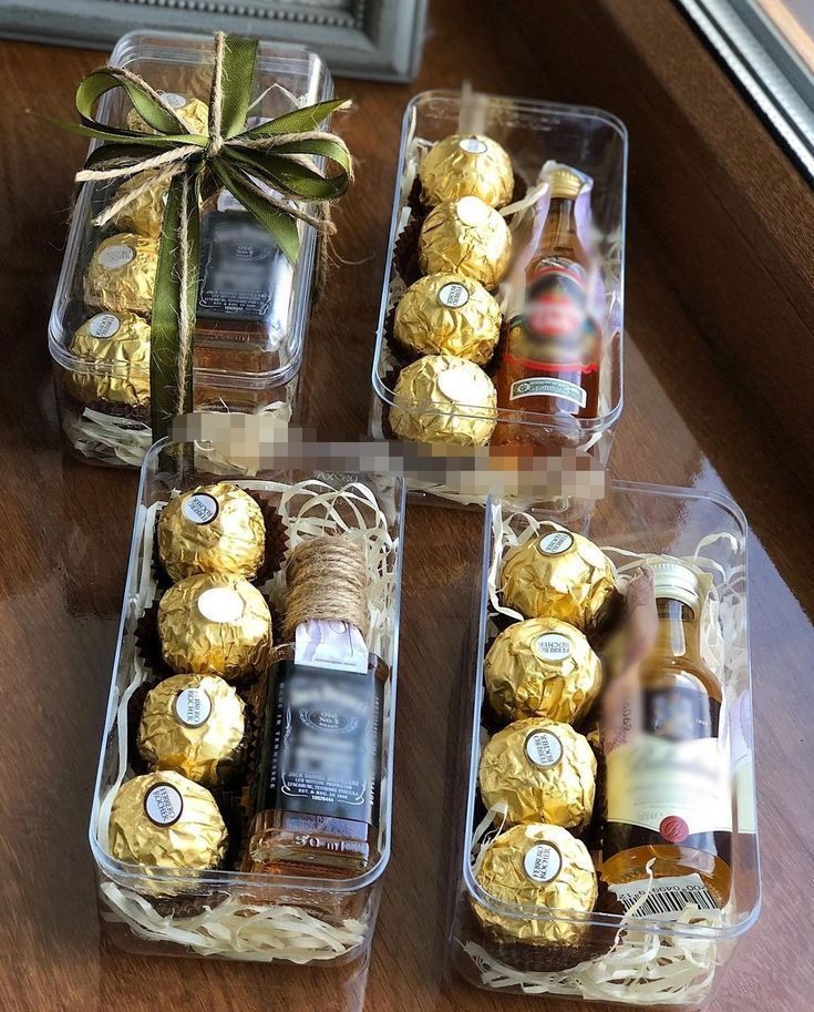 four clear boxes filled with assorted chocolates and bottles of wine sitting on a table