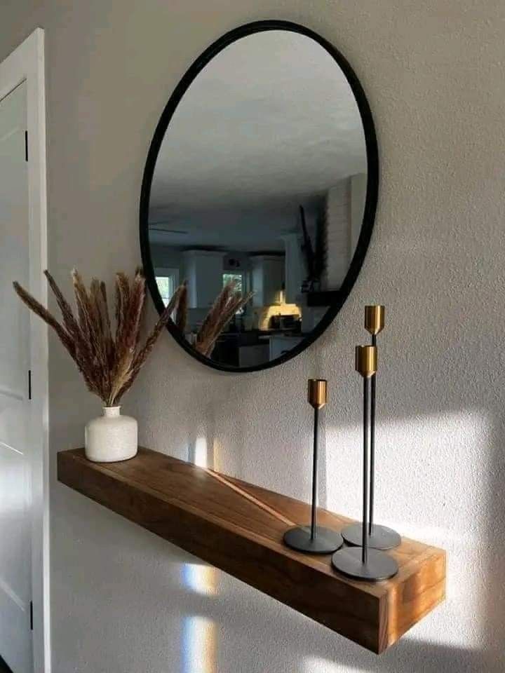 a mirror on the wall above a shelf with two candles and a potted plant