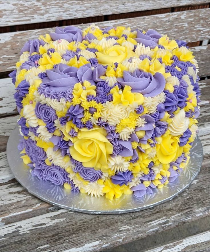 a cake with yellow and purple frosting on a wooden table next to a bench