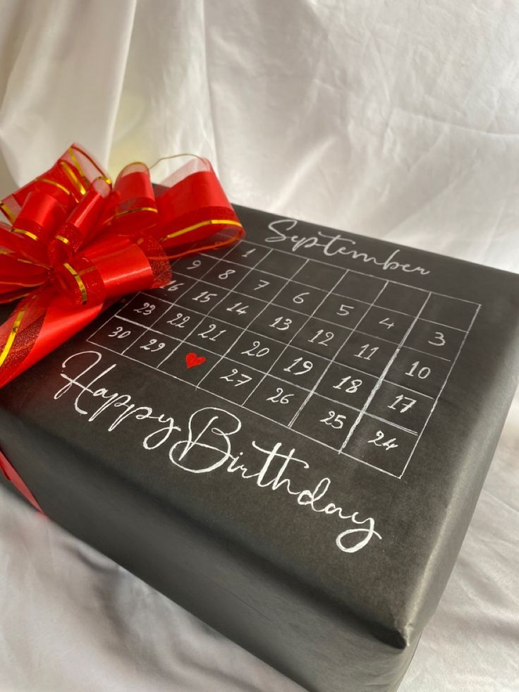 a birthday gift wrapped in black paper with a red bow