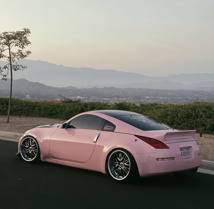 a pink sports car is parked on the side of the road with mountains in the background