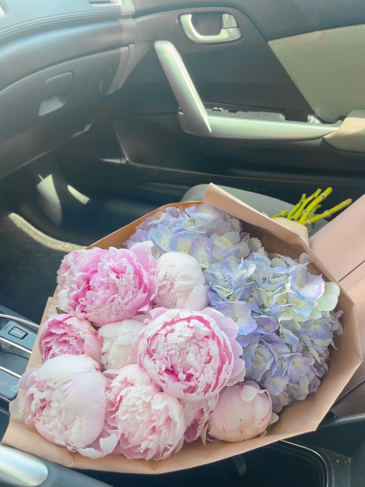 pink and white flowers are in a brown paper bag on the dashboard of a car