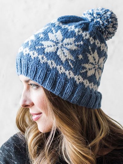 a woman wearing a blue and white knitted hat with pom - poms