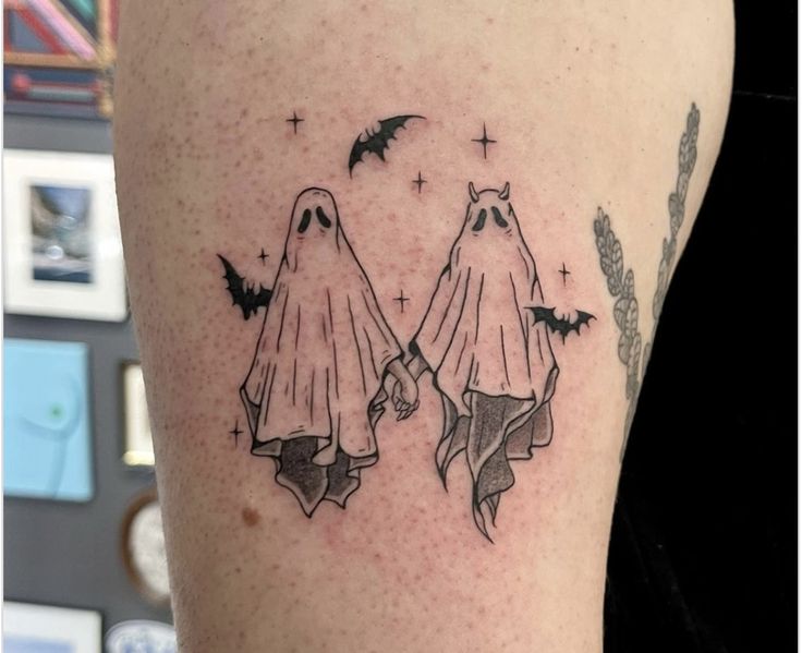 a couple of ghost tattoos on the arm and leg, with bats flying over them