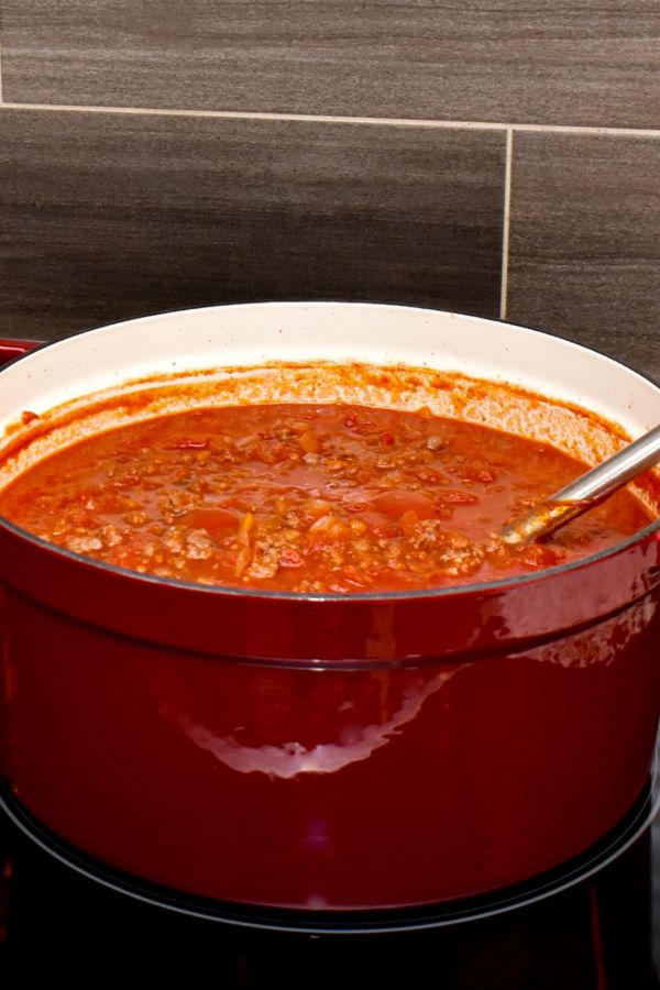 a red pot filled with soup sitting on top of a stove next to a white plate