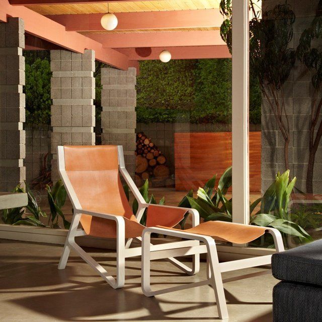 a chair and ottoman sitting in front of a glass wall with plants outside it on the patio