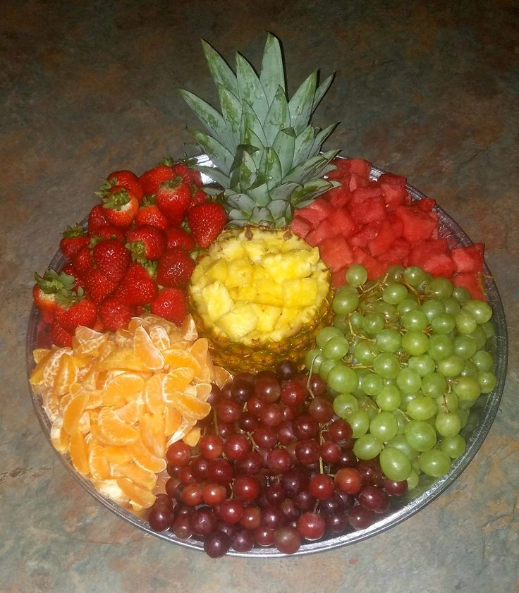 a plate full of different types of fruit on a counter top with pineapples, grapes, strawberries, and oranges