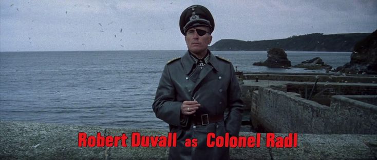 a man in a trench coat and hat standing by the ocean with words robert duval as colonel rad