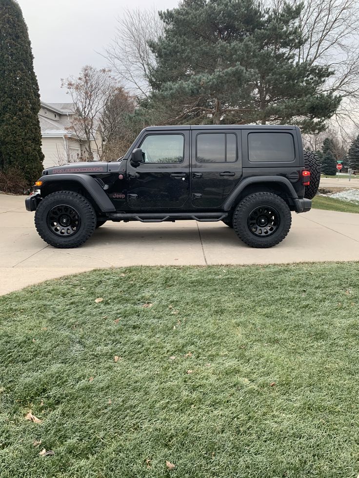 a black jeep parked in front of a house on the side of a road with grass and trees