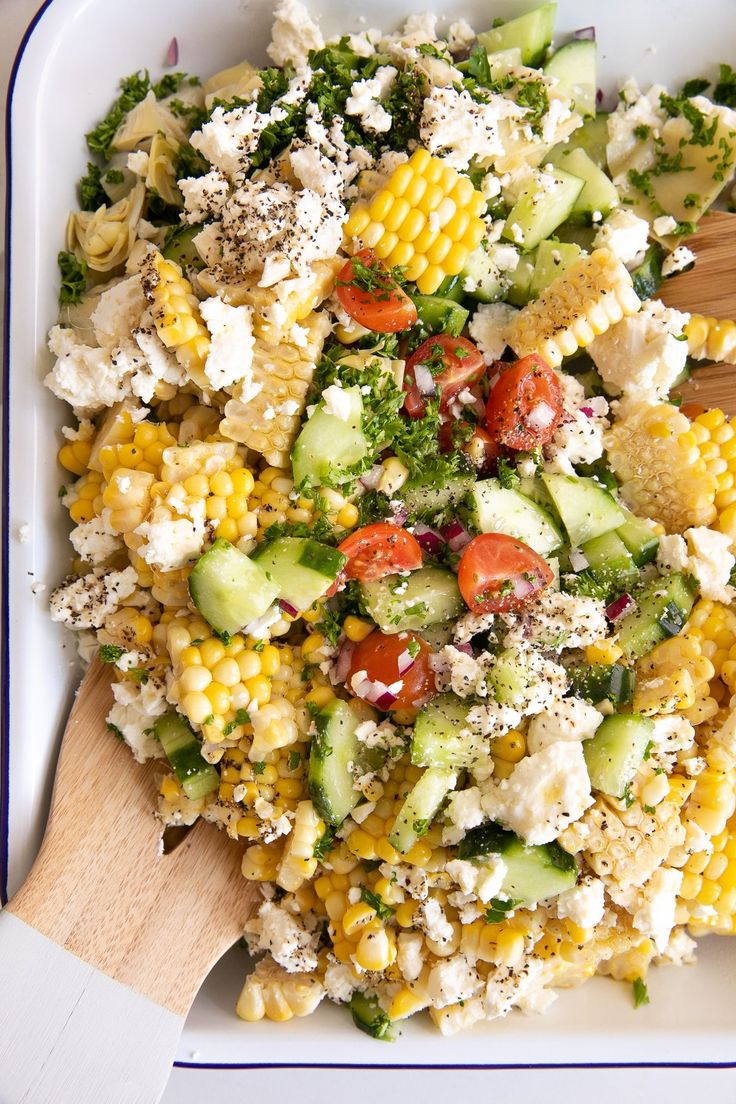 a salad with corn, cucumbers, tomatoes and feta cheese in a white bowl