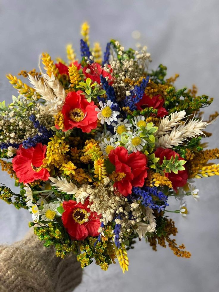 a bouquet of red, white and blue flowers in someone's hand on a gray background