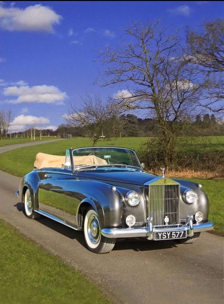 an old fashioned car is parked on the side of the road near a grassy field