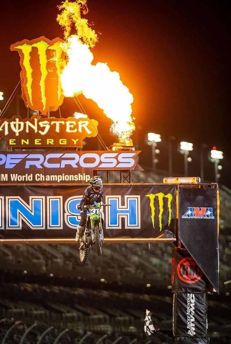 a person on a dirt bike doing a trick in front of a monster energy sign