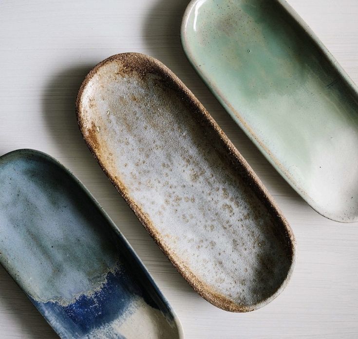 three ceramic dishes sitting on top of a white table next to each other, one blue and the other green