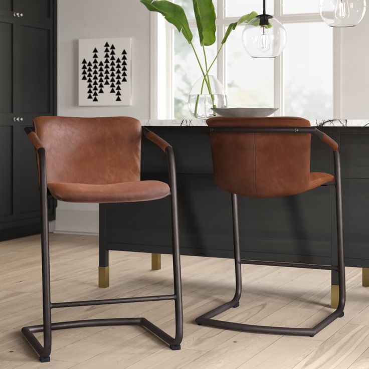 two brown leather chairs sitting next to each other on top of a hard wood floor