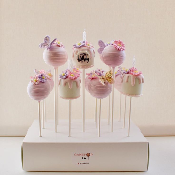 cake pops with pink frosting and flowers on them sitting on top of a white box