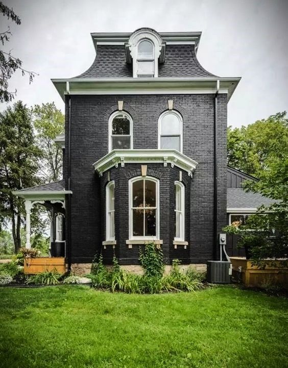 a black house with white trim on the front and side windows, sitting in a grassy yard