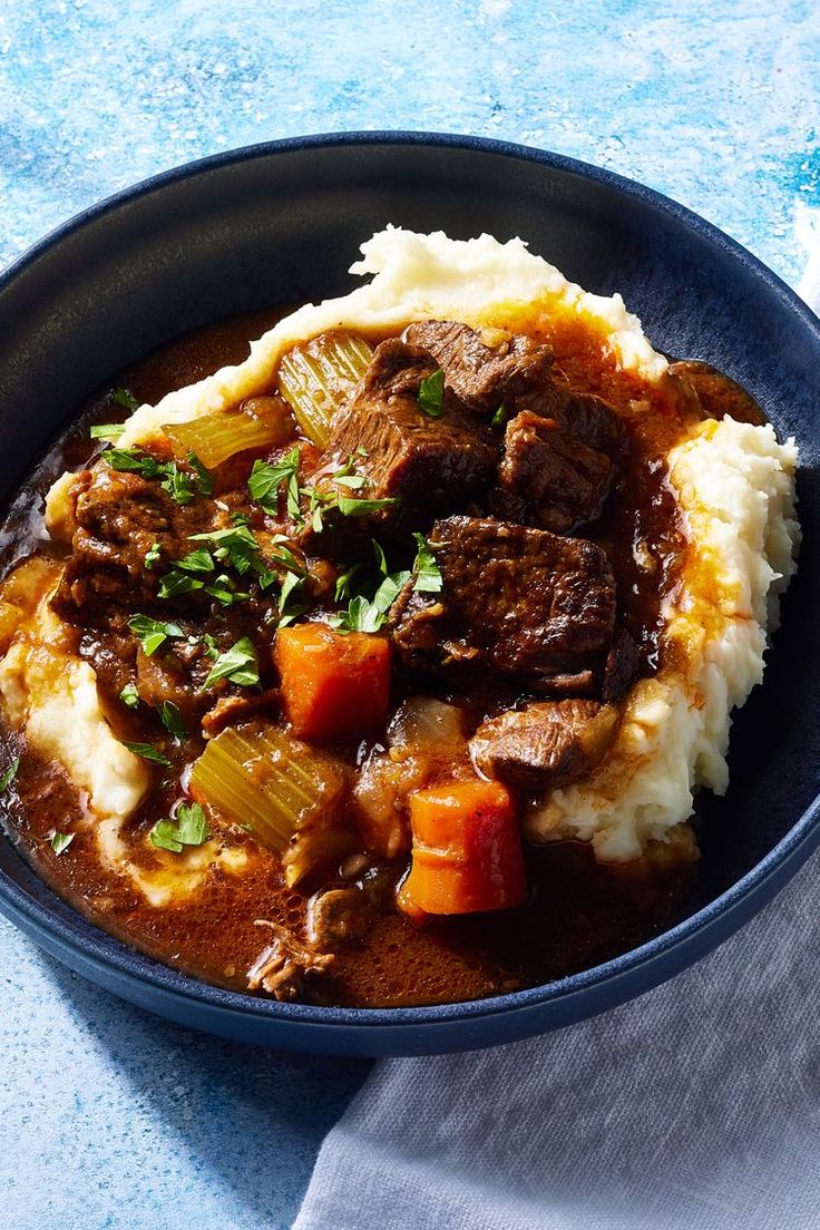 a blue bowl filled with stew and mashed potatoes