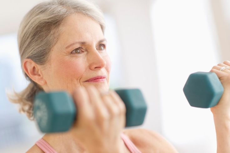 an older woman lifting two dumbs with one hand and the other arm behind her