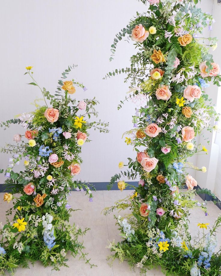 an arrangement of flowers and greenery in front of a white wall with two archways