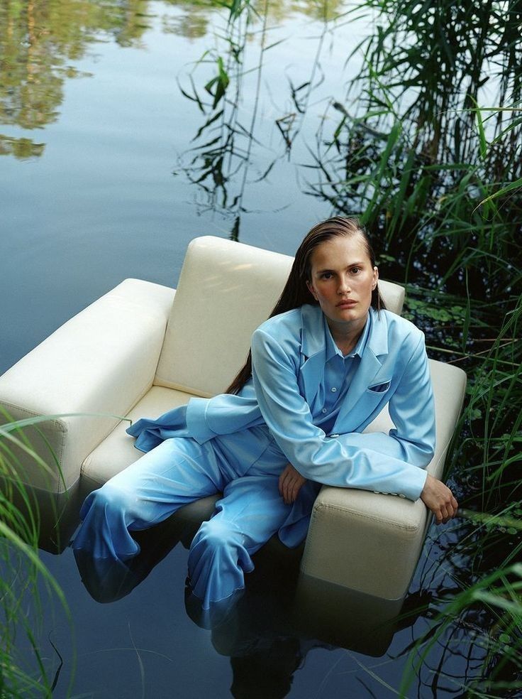 a woman sitting on top of a couch in the water next to tall grass and reeds