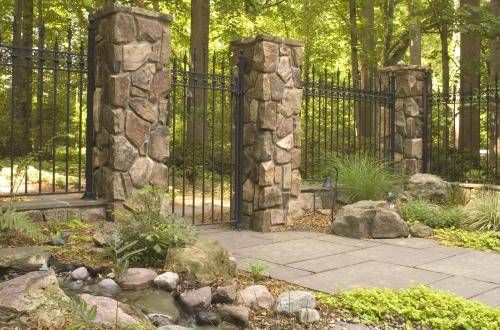 an iron gate in the middle of a garden with rocks and plants around it, surrounded by trees