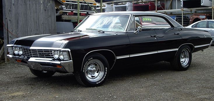 an old black car is parked in front of a wooden building with other cars behind it