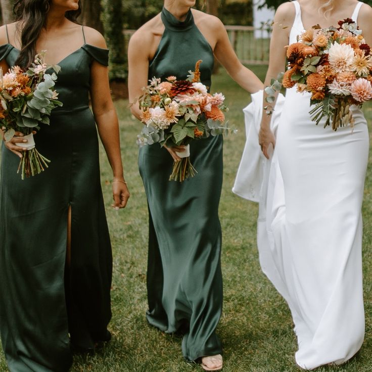 three bridesmaids in green dresses holding bouquets and smiling at each other on the grass