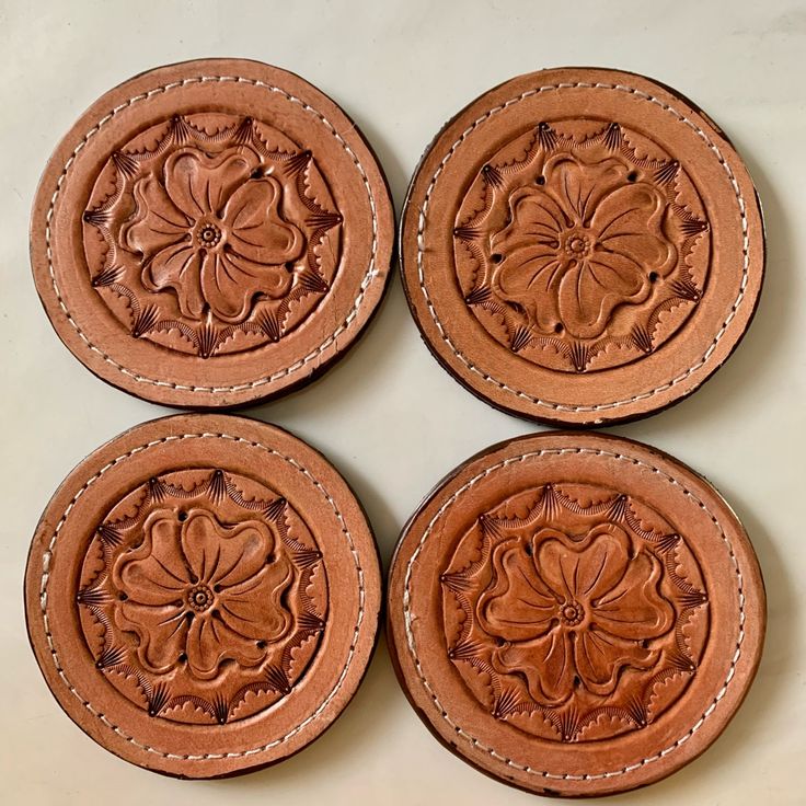 four brown leather coasters with floral designs on them