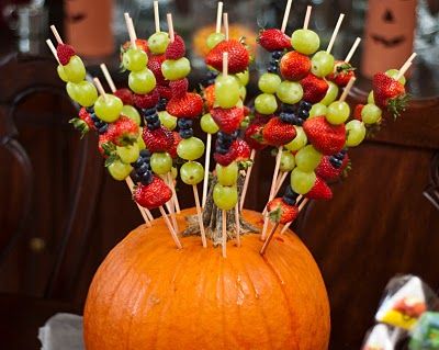 an orange pumpkin with fruit on it and toothpicks sticking out of the top